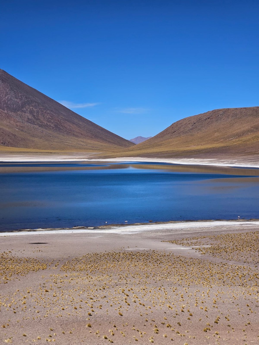 A deep blue lagoon between two brown hills, under a clear sky.