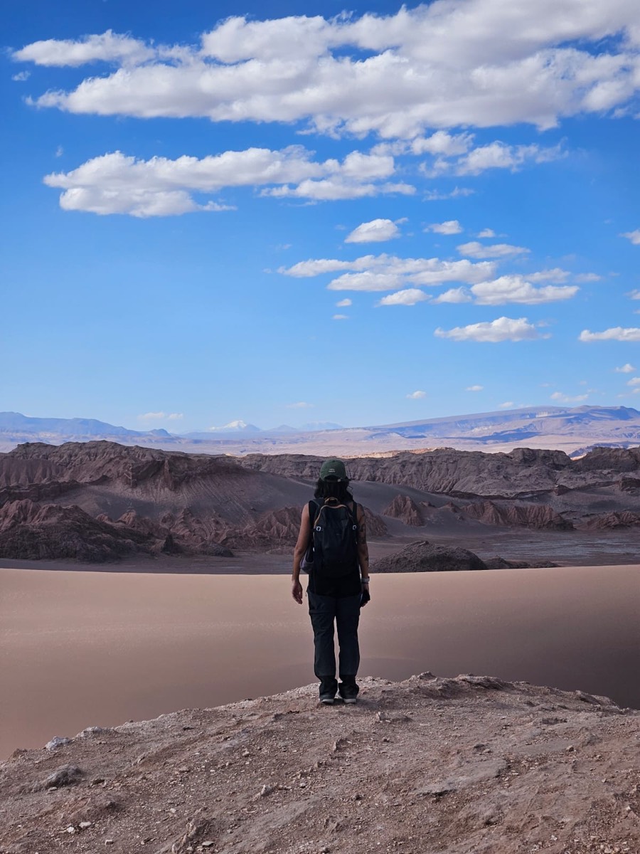 A person with a backpack looking out over a desert valley and dunes.