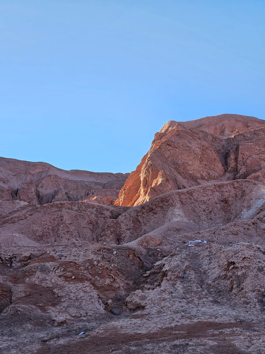 Reddish rock slopes, one face lit by low sun against a blue sky.